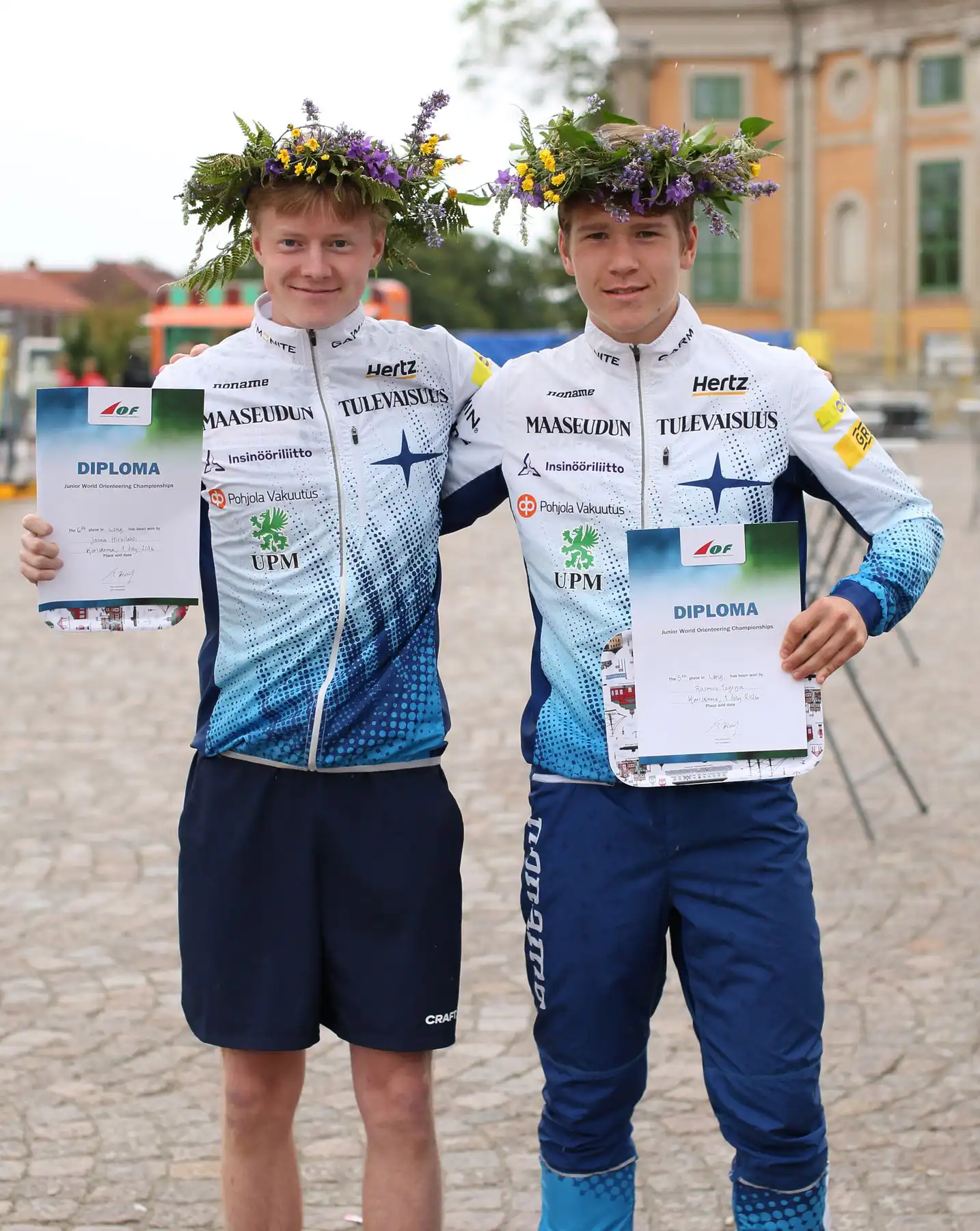Kaksi Suomen nuorten maajoukkueen suunnistajaa seppeleet päässä ja diplomit käsissä.